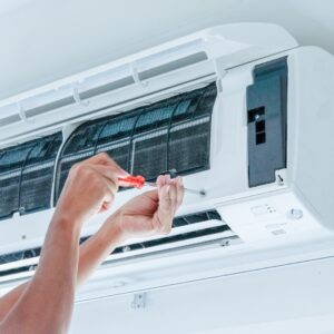 Hands with screwdriver working on an air conditioning unit